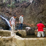 Kepala Desa Gemia, Wahyudin Majid (kiri, bertopi), memantau langsung pembersihan bak penampungan air bersih di Kali Gailafat, Jumat (14/8/2026). (Dok. Pemdes Gemia)